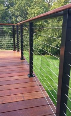 a wooden deck with metal railings in the middle of grass and trees behind it