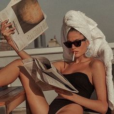 a woman with a towel on her head sitting on a bench and reading a newspaper