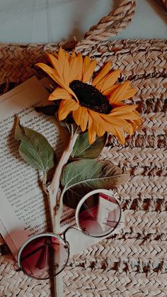 a sunflower and sunglasses on top of an open book next to a straw bag