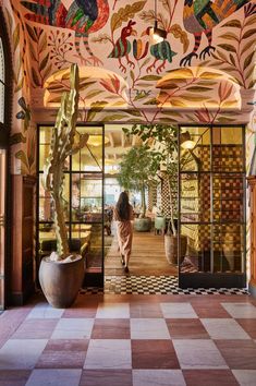 a woman standing in the doorway of a colorfully decorated building with cactuses and cacti on the walls