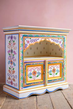 an ornate painted cabinet on a wooden floor with pink wall in the backround