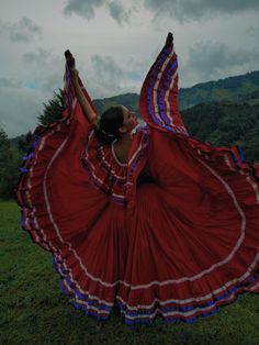 a woman in a red and blue dress is dancing on the grass with her arms outstretched