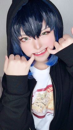 a person with blue hair wearing a black hoodie and posing for the camera in front of a white wall