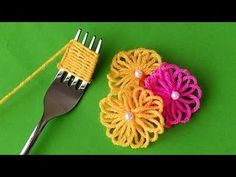 two crocheted flowers and a fork on a green surface with yellow thread next to each other