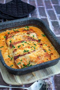 a casserole dish with meat and cheese on a cutting board next to utensils