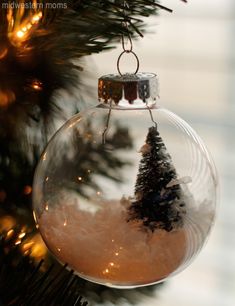 a glass ornament hanging from a christmas tree with snow and trees in it