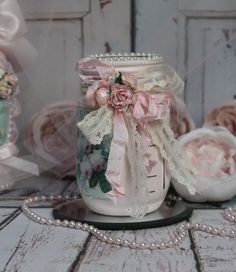 there is a glass jar with pink flowers on it and pearls around the edges, sitting on a table