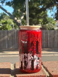 a red jar with black and white designs on it sitting on a brick wall next to a fence