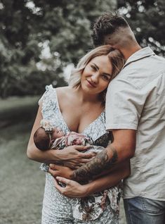 a man holding a baby in his arms while standing next to a woman with tattoos on her arm