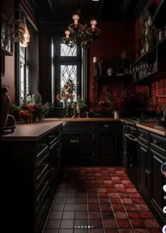 a dark kitchen with red tile flooring and black cabinetry, along with a chandelier hanging from the ceiling