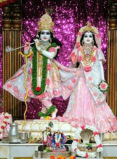 two statues of hindu deities in front of a stage with flowers and garlands on it