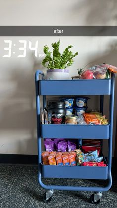 a blue cart filled with food next to a plant on top of a carpeted floor