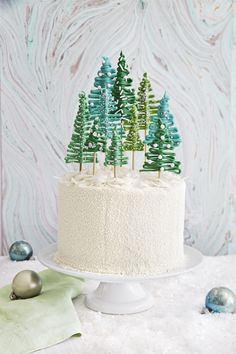 a white cake topped with green trees on top of a table