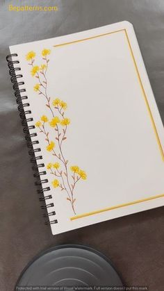 an open notebook with yellow flowers on it sitting on top of a table next to a plate