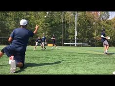 a group of people playing frisbee on top of a grass covered field with trees in the background