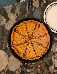 a chocolate chip cookie in a cast iron skillet on a table with plates and utensils