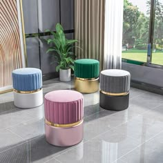 three colorful stools sitting on top of a tiled floor next to a plant in a vase