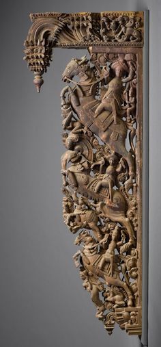 an intricately carved wooden frame with figures on the front and sides, hanging from a gray wall