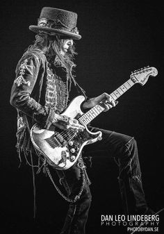 a black and white photo of a man with long hair wearing a top hat playing an electric guitar