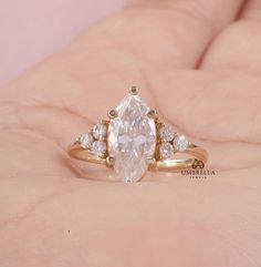 a woman's hand holding an engagement ring with a pear shaped diamond in the center