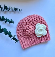 a crocheted pink hat with a white flower on the side and green leaves next to it