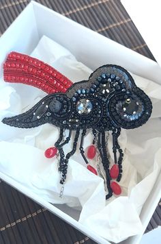 a black and red brooch sitting in a white box on top of a table