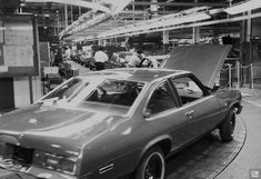 an old photo of a car being worked on in a factory with people working behind it