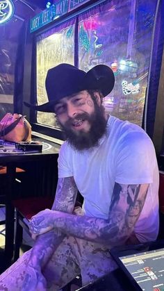 a man with tattoos and a beard sitting in front of a window wearing a hat