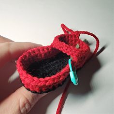 a hand is holding a small crocheted red object with a blue hook in it