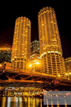 some very tall buildings in the city at night with lights reflecting on the water below