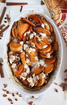 a dish filled with sliced apples and nuts on top of a white table next to cinnamon sticks