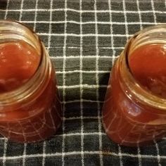 two jars sitting on top of a table covered in brown liquid next to each other