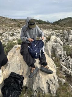 two people sitting on top of a rock in the middle of an open field with backpacks