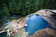 there is a blue pool in the middle of some rocks with trees around it,