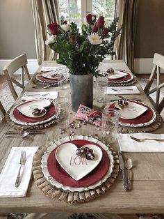 the table is set with red and white plates, silverware, and flowers in a vase