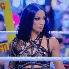 a woman with blue hair is standing in front of a wrestling ring