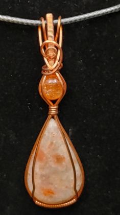 a wire wrapped pendant with an orange stone hanging from it's side on a black surface