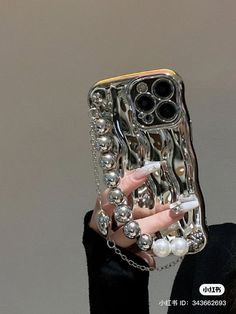 a woman holding up a cell phone case made out of silver balls and chains with her hands