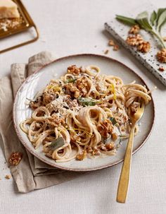 a white plate topped with pasta covered in sauce and nuts next to a napkin on top of a table