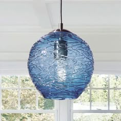 a blue glass light hanging from a ceiling in a room with white walls and windows