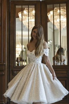 a woman standing in front of a wooden door wearing a short white dress with sequins on it