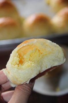 a person holding up a piece of bread in front of a pan filled with rolls