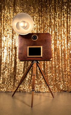 an old fashioned camera on a tripod in front of a gold sequin backdrop