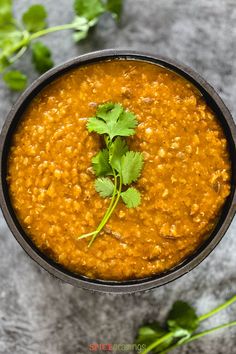 a bowl of soup with cilantro garnish in it on a gray surface