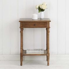 a small wooden table with two vases and flowers on it, against a white wall