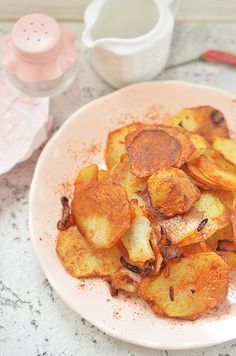 a white plate topped with fried potatoes on top of a counter next to utensils