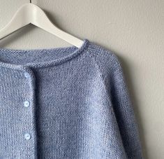 a blue cardigan sweater hanging on a white hanger next to a gray wall