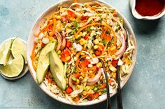 a bowl filled with coleslaw and sliced avocado next to two spoons