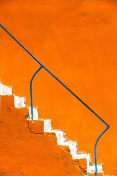 an orange wall with white steps and blue handrail against the wall is painted bright orange