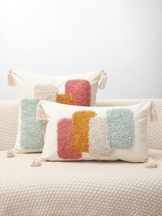 two pillows with tassels sit on a couch in front of a white wall